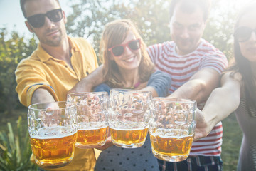 Group of young people enjoying and cheering beer outdoors.