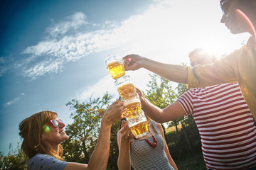 Group of young people enjoying and cheering beer outdoors.