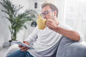 Man holding tablet, surfing online and drinking coffee.
