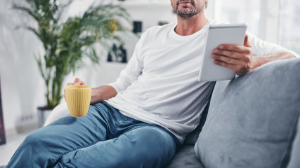 Man holding tablet, surfing online and drinking coffee.