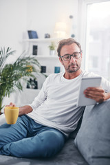 Man holding tablet, surfing online and drinking coffee.