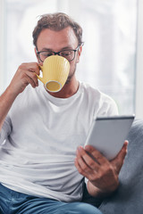 Man holding tablet, surfing online and drinking coffee.