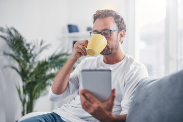 Man holding tablet, surfing online and drinking coffee.