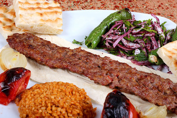 A full-service Turkish-style Orfa kebab complete with green peppercorns and fresh vegetables on a table filled with spicy close-up spices