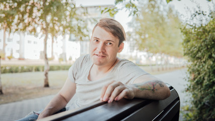 Fototapeta premium A young handsome man in casual clothes sits on a bench in a small alley.