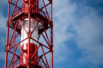 Red and white chemical plant pipe throws harmful poisonous smoke into clear blue sky with copy space. Concept of greenhouse effect and air pollution due to fuel combustion and chemical production.