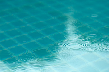 Circles from drops on a blue surface of the water in an open-air pool. Circles on the water.