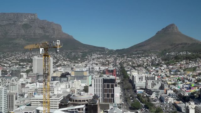 A tower crane operates on high-rise construction site in city business district of Cape Town with Table Mountain as backdrop.