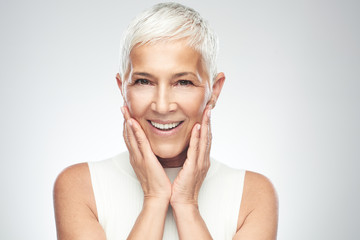 Beautiful smiling senior woman with short gray hair posing in front of gray background. Beauty...