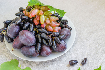 Autumn composition. Grape and plums on the white bowl