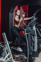 Fototapeta na wymiar Portrait of a young and athletic woman running on a treadmill in a gym. Girl on the simulator, beautiful girl goes in for sports.