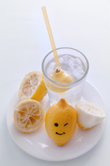 Halved lemon with smile and a glass of lemonade on a white plate on a white background. Making lemonade at home.