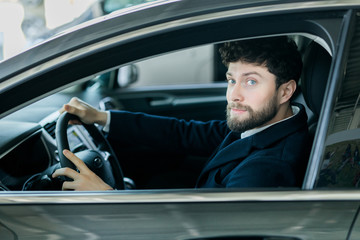 Not leaving without this car. Happy handsome man smiling joyfully while trying out a new car at the dealership