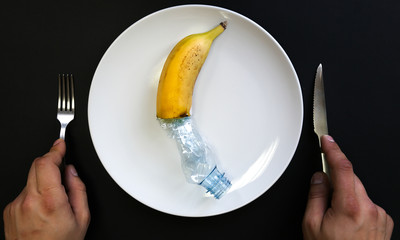 Plastic bottle and banana on the plate. People eating polluted food. Environmental issue....
