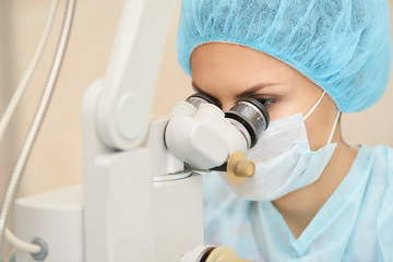 Pretty doctor woman portrait. Ophthalmology laser microscope operation. Clinic room. Patient eye...