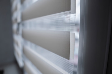 Details of white fabric roller blinds on the white plastic window in the living room. Close up on roll curtains indoor.