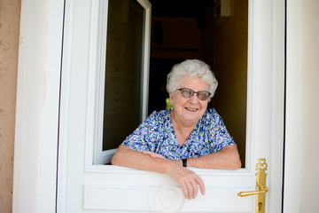 elderly senior woman opening front door of house and welcoming people at home