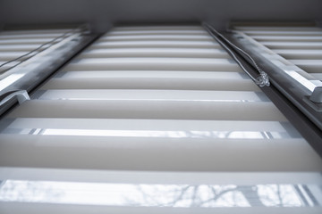 Details of white fabric roller blinds on the white plastic window in the living room. Close up on roll curtains indoor.