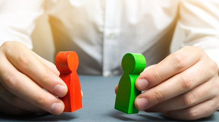 A man holds in his hands the red and green figures of people facing each other. The search for a...