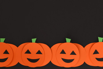 Halloween flat lay background with orange paper crafted carved pumpkins with faces on black background with copy space