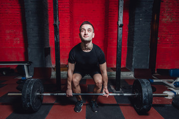 Obraz na płótnie Canvas Young athlete dressed in black t-shirt. During this time, he trains crossfit to the gym. At the same time, it raises the bar with maximum effort.