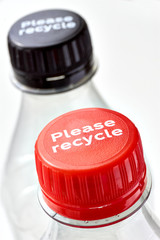 Plastic bottles and black and red bottle caps with please recycle message against a white background. Concept of plastic pollution. Vertical image.