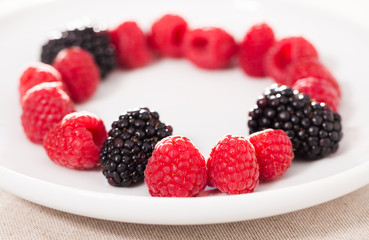 raspberries and blackberries laid out on a white plate in circle