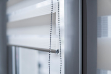 Details of white fabric roller blinds on the white plastic window in the living room. Close up on...