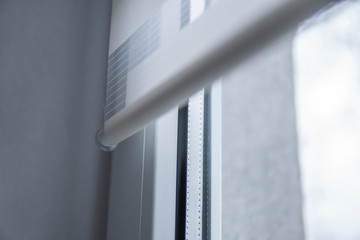 Details of white fabric roller blinds on the white plastic window in the living room. Close up on...