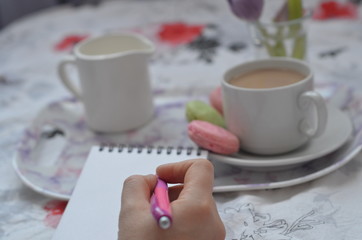 tray with paper sketchbook, smartphone and spring flowers on pink bedding. Relaxing, or working, or writing diary or blog in bed at home.