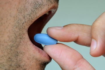 Hand of man holding blue pill. Closeup of a man taking blue medicine pill. Mouth view, illness. Medicine concept of viagra, medication for stomach, erection, sleeping, digestive or drugs - obrazy, fototapety, plakaty