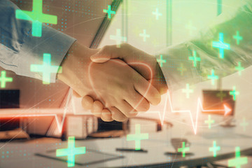 Multi exposure of heart icon hologram on office background with two men handshake. Concept of medical education