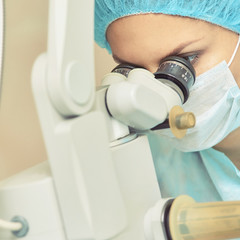 Pretty doctor woman portrait. Ophthalmology laser microscope operation. Clinic room. Patient eye...