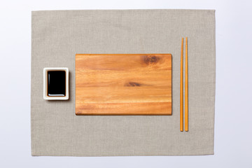 Empty rectangular brown wooden plate with chopsticks for sushi and soy sauce on grey napkin background. Top view with copy space for you design