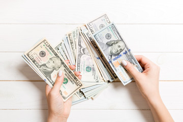 Top view of female hands counting money. One hundred and other dollar banknotes on wooden background. Business concept