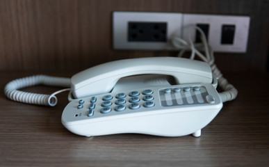 White vintage telephone with grey battoms on a brown table in hotel.
