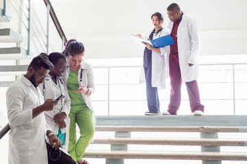 a group of doctors on the steps in the hospital. Young people of mixed race, in medical clothes, examine X-rays, use a smartphone