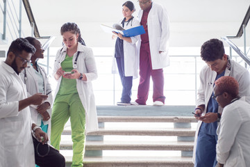 a group of doctors on the steps in the hospital. Young people of mixed race, in medical clothes, examine X-rays, use a smartphone