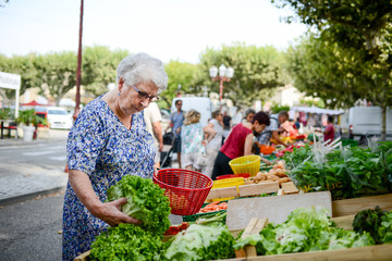 elderly senior woman buying fresh vegetables and fruits in farmer's market during a summer day in...