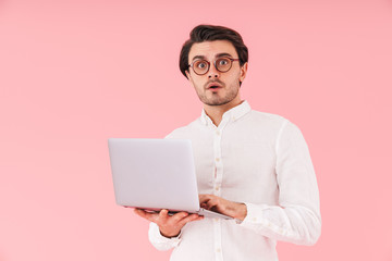 Image of handsome confused man wearing eyeglasses typing on laptop and looking at camera
