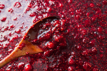 raspberry jam is stirred with a wooden spoon.