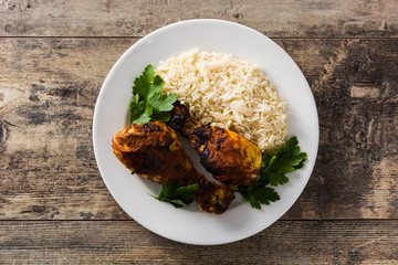 Roasted tandoori chicken with basmati rice in plate on wooden table. Top view