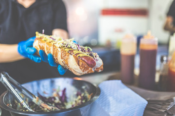 Close up of chef holding fresh hot dog with grilled sausage.