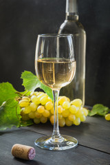 Bottle of white wine with wineglass, ripe grape on black wooden table. Close up.