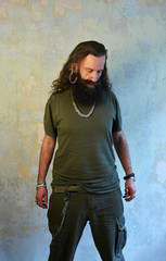 Guy with long hairs and beard standing in a empty room, in front of a wall