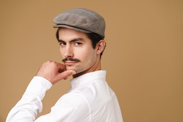 Image closeup of strict mustached man wearing hat looking at camera and touching his chin