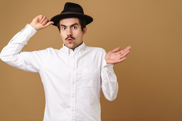 Image closeup of stylish mustached man wearing shirt looking at camera and holding hat