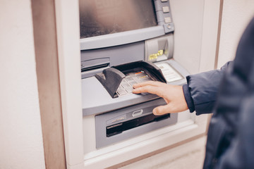 Closeup of male hands using smart phone while typing on ATM, bank machine 