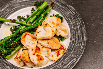 Cooked broccolini with turkey fillet on a plate, top view.