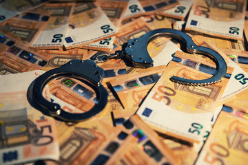 financial crime concept - handcuffs on cash money